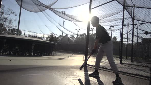 A young man practicing baseball at the batting cages.