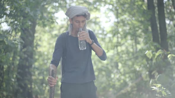 Young Cautious Refugee Walking in Sunlight in Green Summer Forest and Drinking Refreshing Water