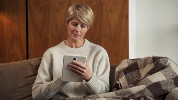 Portrait of a Middleaged Woman Sitting on a Cozy Sofa and Using a Tablet Computer at Home