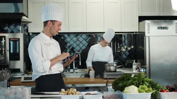 Restaurant kitchen: portrait of male and female cooks. Male Chef checks the availability