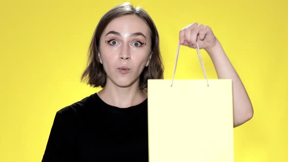 Smiling young woman holding credit card on yellow background.