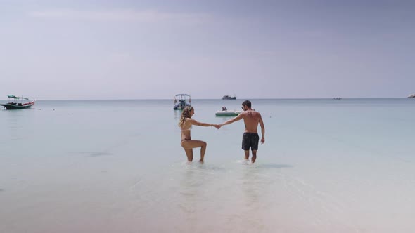 A Backside View of a Happy Cheerful Couple Having Fun Running to the Sea Together and Doing Splashes