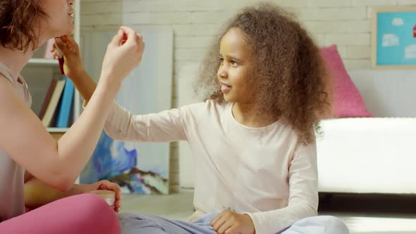 Joyous Woman Teaching Little African Girl to Apply Powder alt