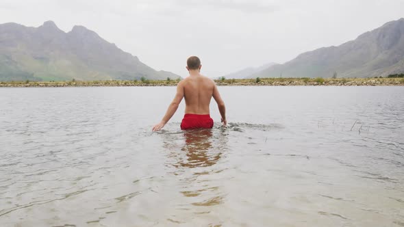 Caucasian man having a good time on a trip to the mountains, wearing bathing trunks and jumping into