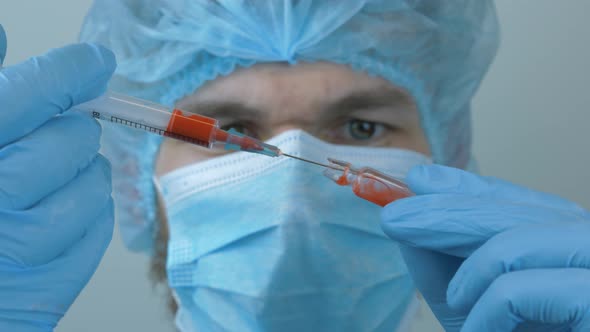 Medical doctor in protective clothes filling test tube with blood samples wearing blue mask and cap