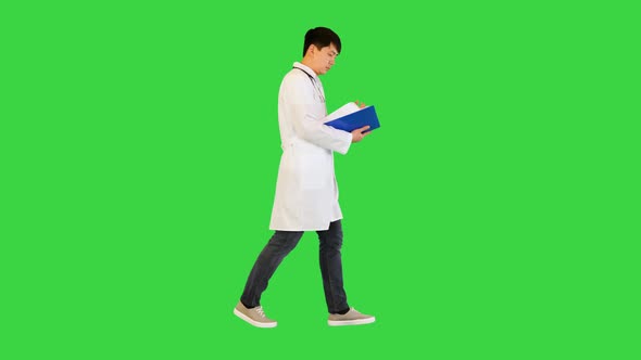 Young Asian Doctor Walks Studying a Document on a Green Screen Chroma Key