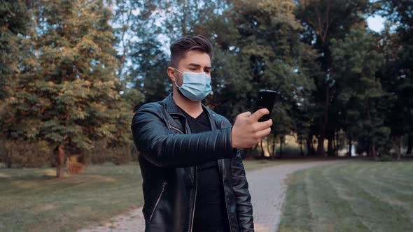 A Young and Handsome Boy Takes a Selfie with His Mobile Phone, Wearing a Surgical Face Mask.