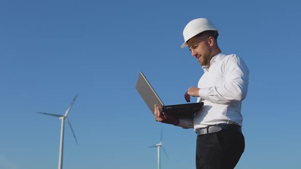 A Male Engineer in a White Helmet and a Classic Shirt Inspects the Power Plant's Capacity and Makes