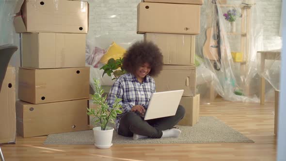 Black Woman with an Afro Hairstyle Sitting on the Floor and Using a Laptopconcept of Moving