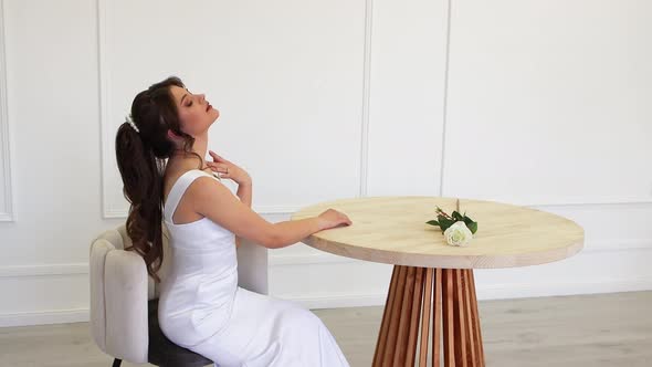 A Blackhaired Beauty in a Wedding Dress Poses While Sitting at a Table