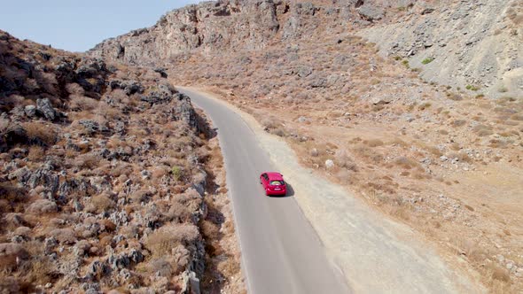 Aerial shot car driving along the narrow coastal road above rocky shore towards volcanic mountains
