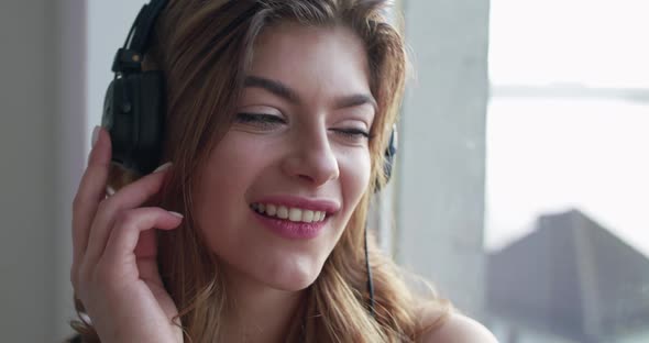 Woman with Headphones Touches the Earcups Dreams Gazes at Camera and Flirts