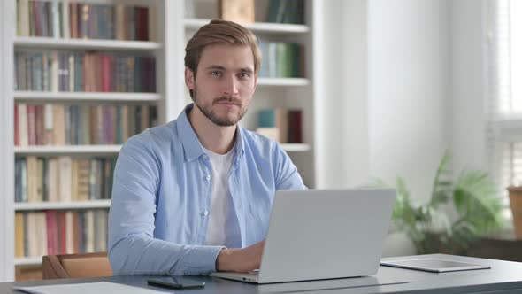 Man Smiling at Camera While Using Laptop in Office