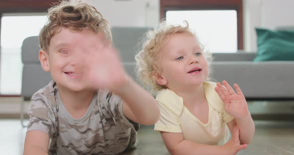 Close Up of a Little Boy and a Little Girl Who are Laying on the Floor and Waving Hands Looking to