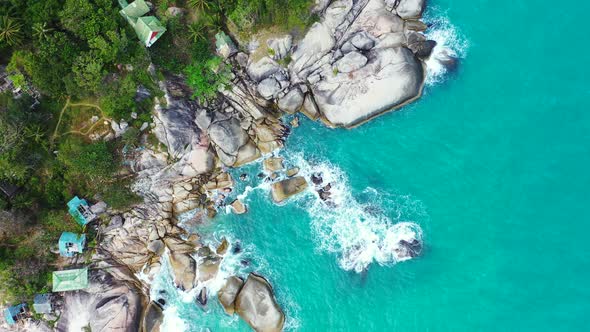 Beautiful cliffs caved by turquoise sea water on shore of tropical island, beach cabins built on hig