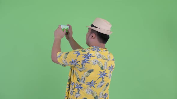 Rear View of Young Overweight Asian Tourist Man Taking Picture with Phone