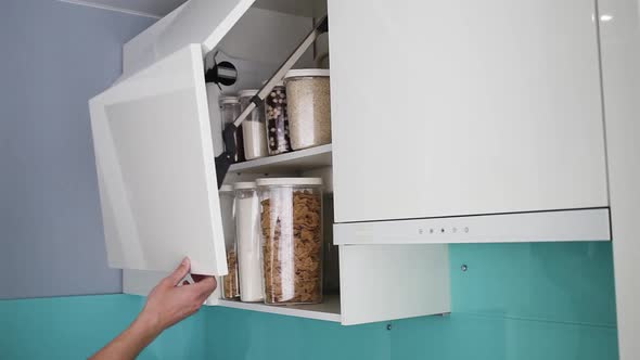 A male hand opens and closes a cabinet in a modern white kitchen without handles.