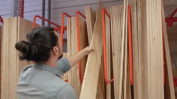 Young Man Selecting Wood Boards in a Hardware Store or Warehouse