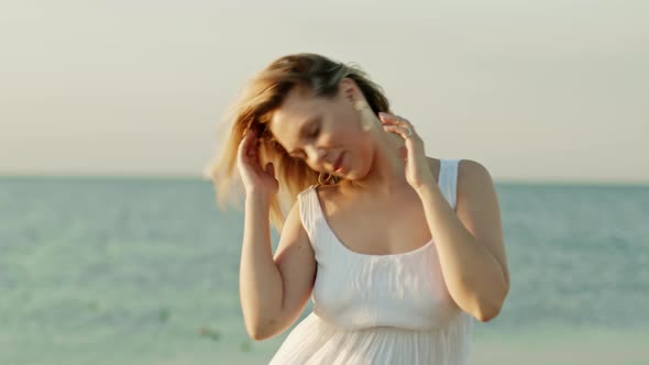 Woman in White Dress with Blonde Hairstyle Dancing Head on Sea Background. Girl Moves To Rhythm of