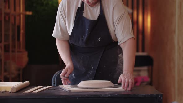 An Eldery Woman Cutting a Piece of Clay By the Shape