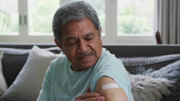 Portrait of senior man touching bandage on arm and smiling while sitting at home after vaccination