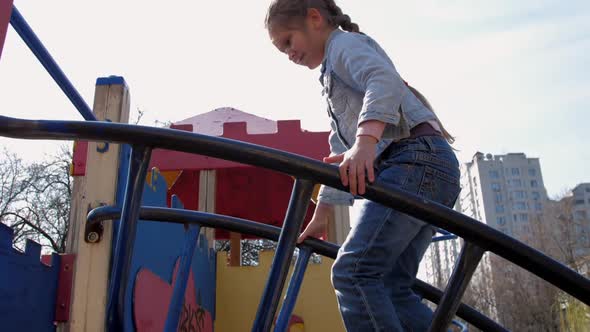 Junior Schoolgirl in Pullover Climbs Up Metal Attraction