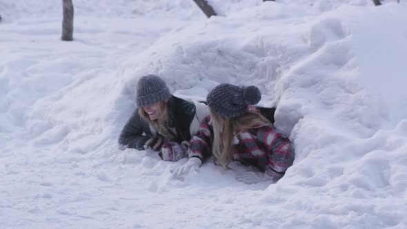 Two girls climbing out of snow cave with dog