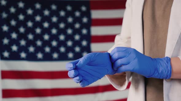 A Woman Wears Protective Rubber Gloves Against the Background of the American Flag