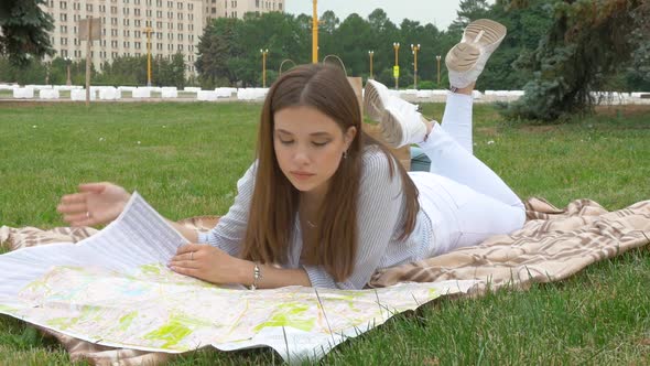 Brown-haired with Long Hair Is Lying on the Rug and Considering a Paper Map
