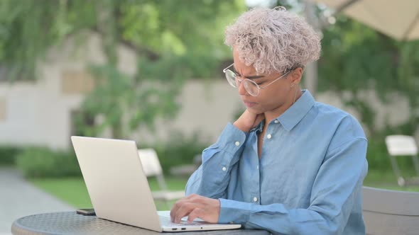 Young African Woman with Neck Pain Working on Laptop in Outdoor Cafe