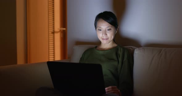 Woman sit on sofa and work on computer at night