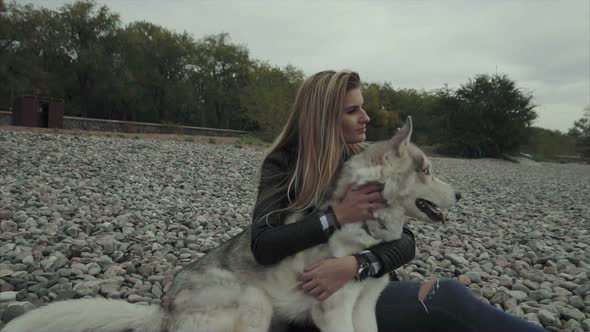 Young Pretty Woman with Siberian Husky Dog Sitting on the River Bank