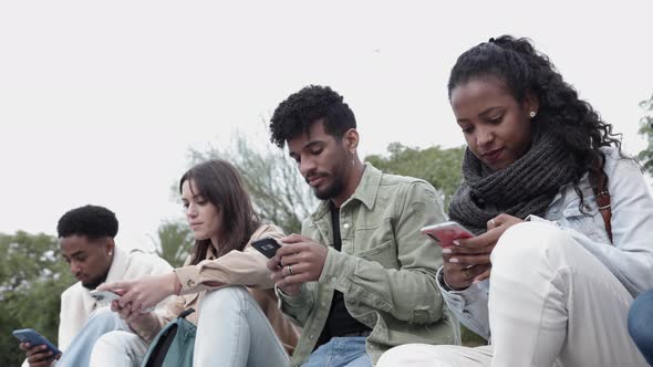 Group of Teenage Students Using Smart Phones While Sitting Together Outdoors