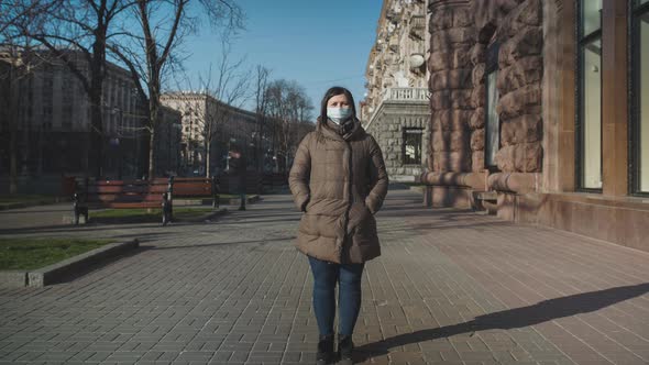 A Girl in a Medical Mask Stands in the Center of the City Space