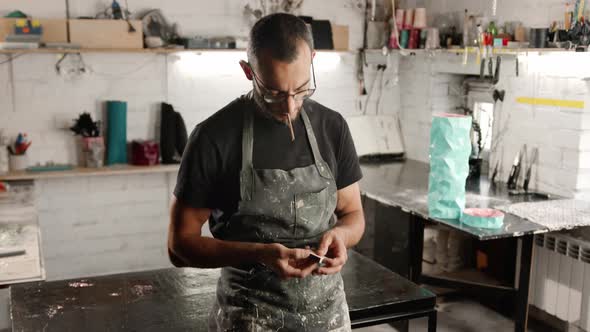 Male portrait: A man smokes a cigarette in a workshop.. The sculptor is tired and resting.