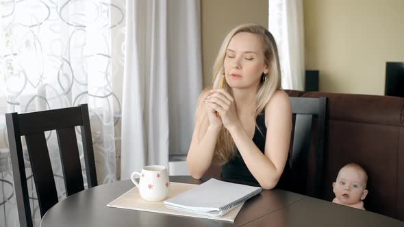 Young Pregnant Woman Sitting at Table in Home Interior, Baby Is Crawling Near.