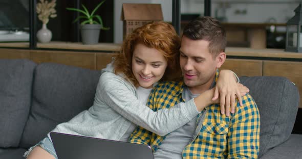 Young Man and Woman in Casual Clothes, Relaxing on a Sofa, Using Laptop