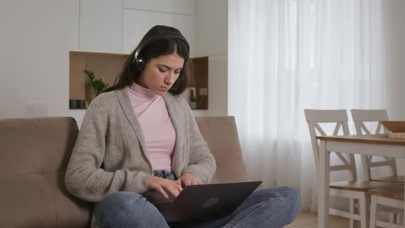 Young 20s Caucasian Woman Listening to Online Course While Working on a Laptop in Bright Apartment