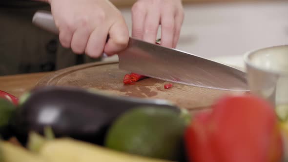 Handheld view of woman cutting chili pepper into slices