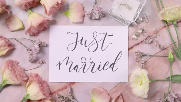 JUST MARRIED card on a marble table near pink flowers top view zoom in