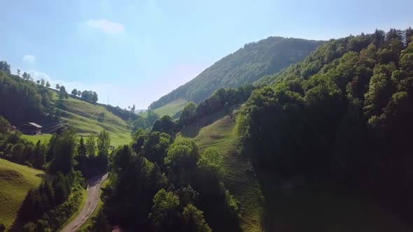 Pass road on a hill in the summer. Aerial shot of the road with cars driving on it and some houses.