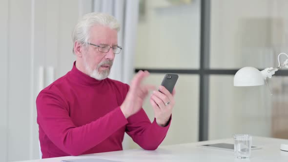 Old Man Celebrating Success on Smartphone at Work