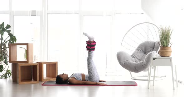 Pretty fitness black woman in sportswear practicing donkey kick exercise with ankle weigh.