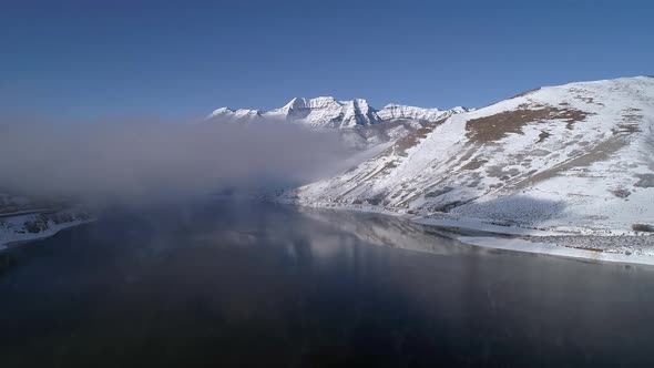 Aerial view flying over lake towards clouds in winter landscape