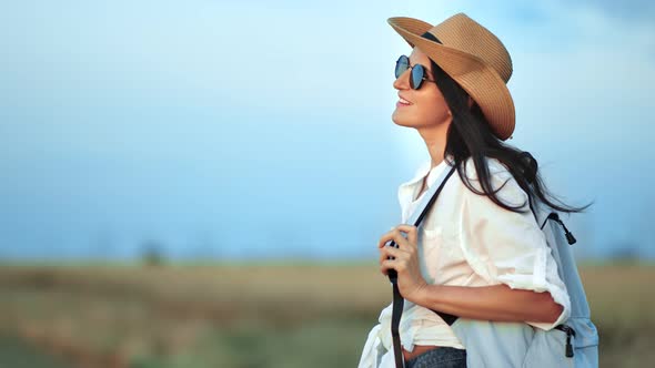 Relaxed Beautiful Travel Backpacker Woman in Hat and Sunglasses Enjoying Beauty of Nature at Sunset