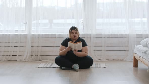 A Fat Woman Sitting on the Floor and Reading a Book at Home