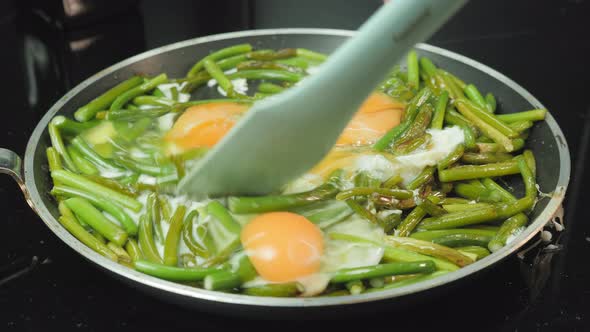 Flipping eggs and green beans in frying pan.