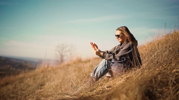 A Young Adult Woman Using Her Smartphone While Sitting on the Hill