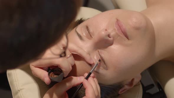 Cosmetologist is Painting Eye Lashes of the Client Caucasian Woman During Lamination Procedure