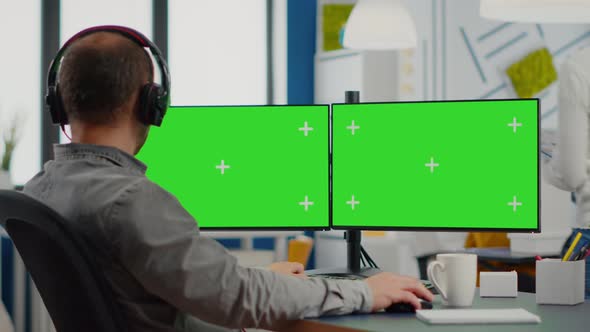 Employee with Headphones Working in Dual Monitror Setup with Green Screen
